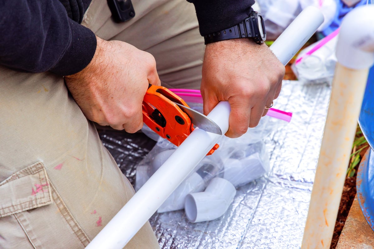 A plumber cutting a PVC pipe surrounded by fittings